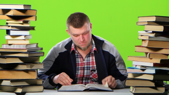 Man Sitting at Table with Books and Reading an Interesting Chapter. Green Screen