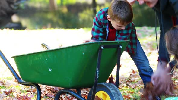 Family picking up autumn leaves and putting in a wheelbarrow