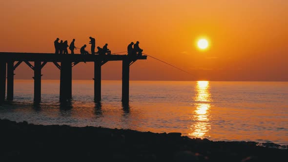 Silhouettes of Fishermen with Fishing Rods at Sea Sunset Sitting on the Pier. Slow Motion