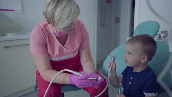 Dentist in Medical Mask and Gloves Ready To Checking Tooths of Little Carefree Boy Sitting