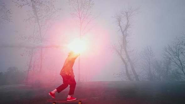 Young Man is Riding a Skateboard in the Evening Holding a Burning Torch in One Hand