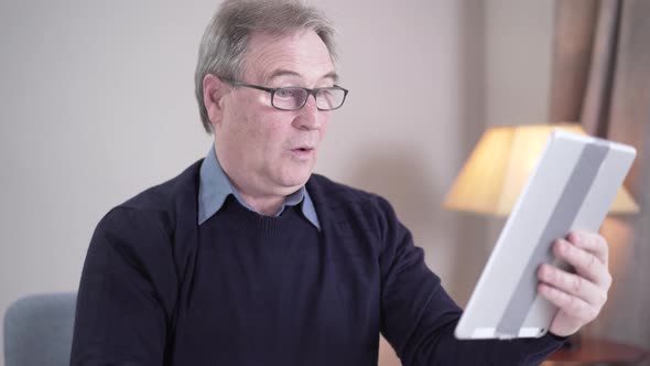 Positive Senior Caucasian Man Scrolling Tablet Screen and Waving at Selfie Camera