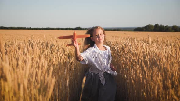 Cute Girl Playing with Toy Airplane in the Wheat Field at Sunset. Silhouette of Child Playing with