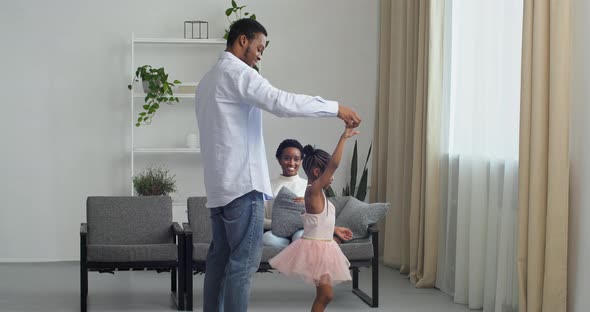 Loving Afro American Dad Holding Hand of His Daughter Dancing with Cute Little Child Princess Wears