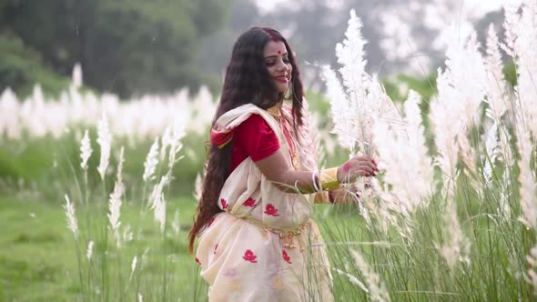 An innocent and playful married Indian bengali woman wearing saree plays with the long white grass i