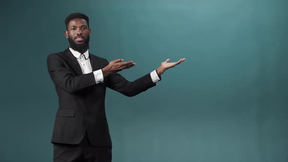 A Black Bearded Man in a Tuxedo is Posing Standing with with Outstretched Arms and Looking at the