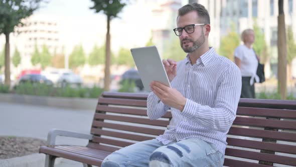 Online Video Chat on Tablet By Young Adult Man Sitting Outdoor on Bench