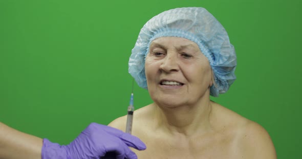 Smiling Elderly Female Lady in Protective Hat Scared of Syringe with Medicines