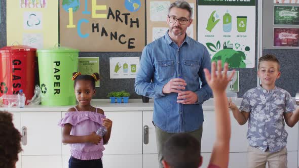 Diverse teacher and schoolchildren standing in classroom learning about recycling trash