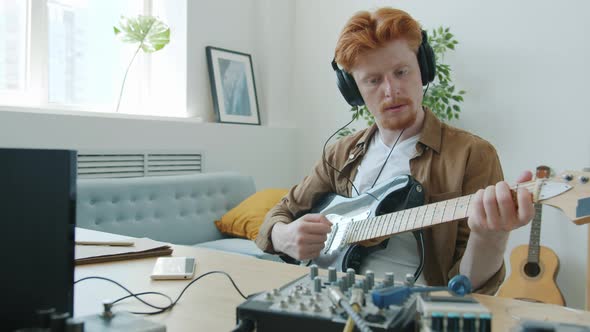 Slow Motion Portrait of Attractive Guy Musician Playing Guitar Wearing Headphones Adjusting