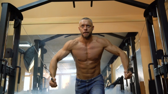 Bodybuilder Is Working On His Chest With Cable Crossover In Gym. Smoke on Background