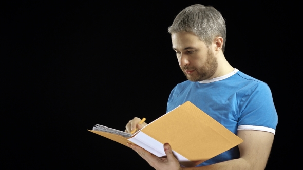 Handsome Man in Blue Tshirt Looking Through Papers in Yellow Folder