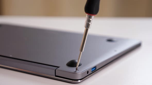 Closeup of Unscrewing Bolts with a Screwdriver on a Silver Laptop