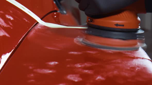 Detailing a red sports car with a red polishing machine. Close up.