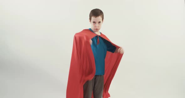 Boy with a superhero cape pretends to fly on a white studio background