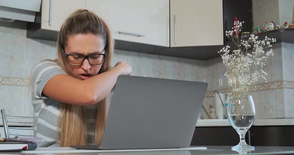 Young Woman in Glasses Coughs Into Elbow Sitting at Laptop