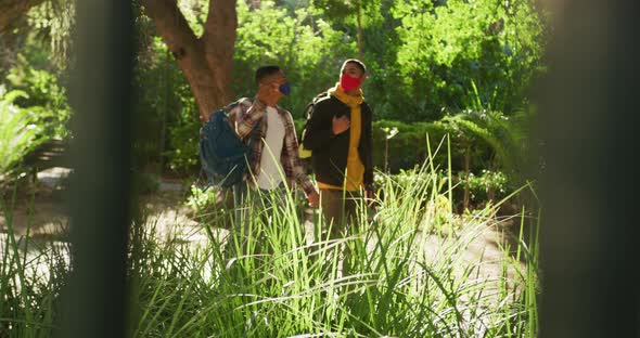 Two happy mixed race male friends walking and talking in park with backpacks