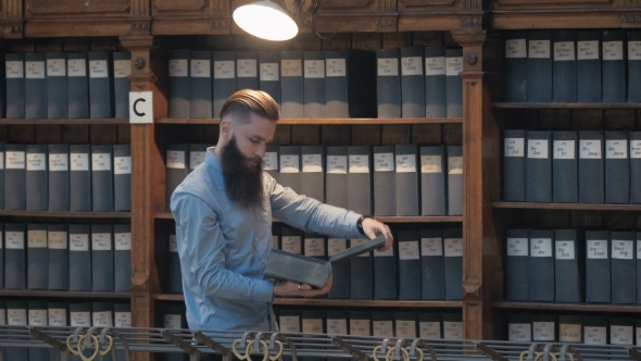 Attractive Librarian Holding a Pile of Books Standing in Library