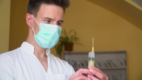 Young Doctor in Protective Mask Preparing Syringe for Injection. Close Up of Young Intern in