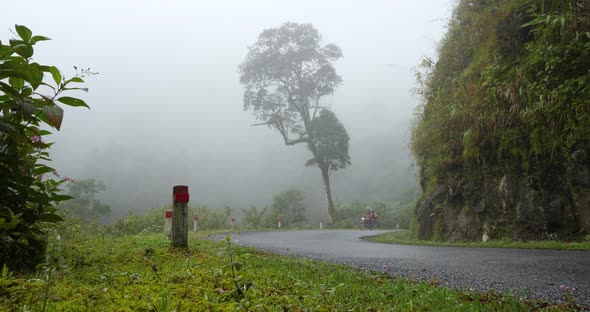 Couple on a Motorbike Traveling on a Paved Curvy Road in the Misty Mountains.