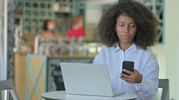 African Woman Using Smartphone and Laptop in Cafe 