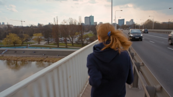 Nice Young Lady with Ponytail in Sportswear Is Running on a Bridge in the City