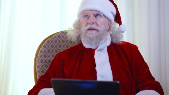 Concentrated Bearded Senior Man in Santa Clause Costume Thinking Surfing Internet on Tablet