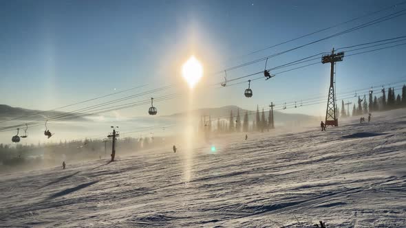 Ski Lift Cabins Move Above Tourists Skiing Along Snowy Slope