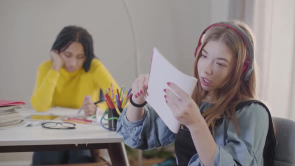 Teenage Caucasian Girl in Earphones Throwing Away Notebook and Singing. Cute Teen Resting As Her