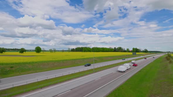 Beautiful top view of highway with moving cars. Rapeseed fields with white clouds against sky.