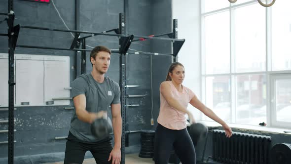 Young Couple Training in Gym Weightlifting Squatting with Kettlebells Together