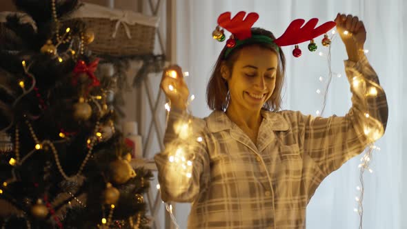 Portrait of Happy Cheerful Pretty Woman Wearing Pajama and Reindeer Antlers Headband Dancing with