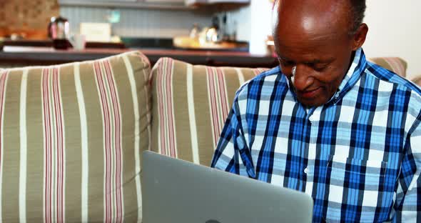 Senior man talking using laptop in living room