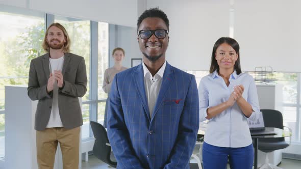 African Young Boss Smiling at Camera with Diverse Team Applauding on Background