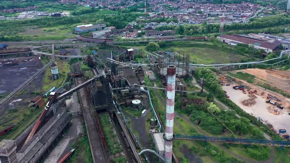 Aerial top-down view of abandoned steel factory. Flying around chimney revealing the city behind