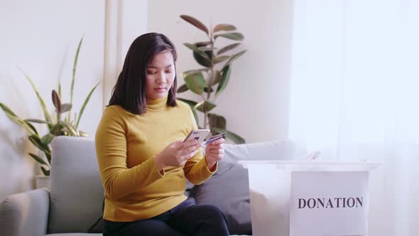Asian woman pressing phone using a credit card to pay online to reserve donation box delivery. Conce