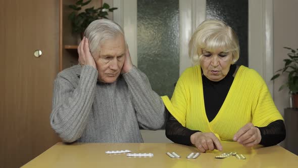 Old Senior Grandparents Looking at Pills, Tablets in a Blisters on Table at Home