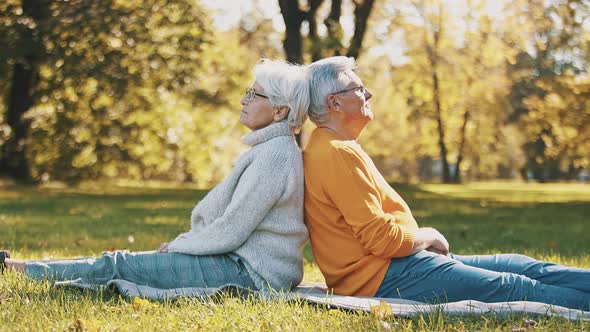 Romance at Old Age. Elderly Retired Couple Sitting Back To Back in the Park in Autumn