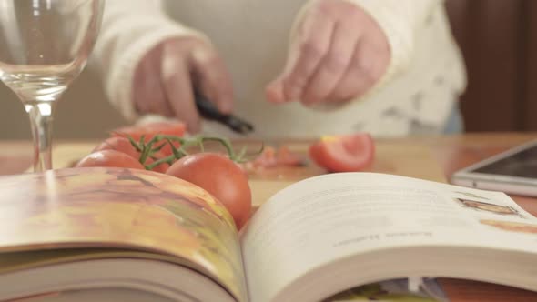 Hands cutting fresh vine tomatoes in kitchen with recipe book close up shot