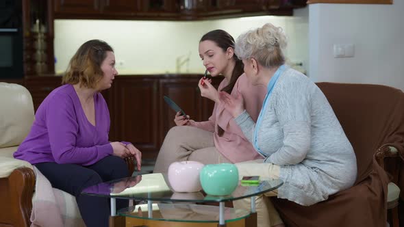 Wide Shot of Slim Beautiful Millennial Woman Applying Lipstick As Mother and Grandmother Giving