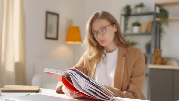 Young Woman in Glasses Looking at Notebook at Home