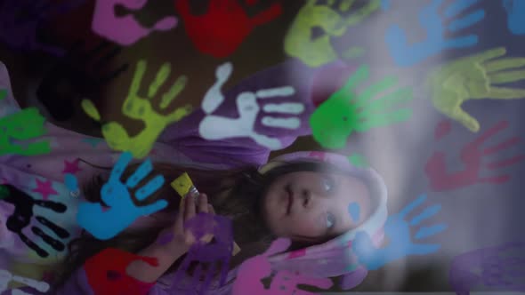 Vertical Video. School Girl in Pajamas Paint with Palms on the Window.