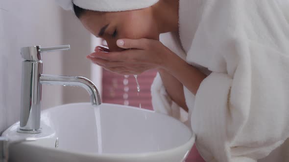 Closeup Young Happy Woman with Towel on Head in White Bathrobe Washes Face in Bathroom Refreshes