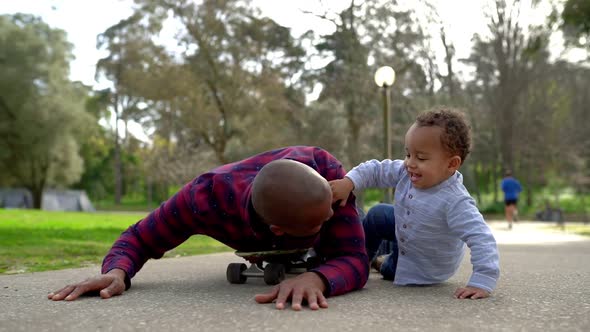 Mixed-race Little Boy and Father Playing with Scateboard