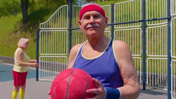 Senior Man Grandfather Posing with Ball Looking at Camera Outdoors on Basketball Playground Court