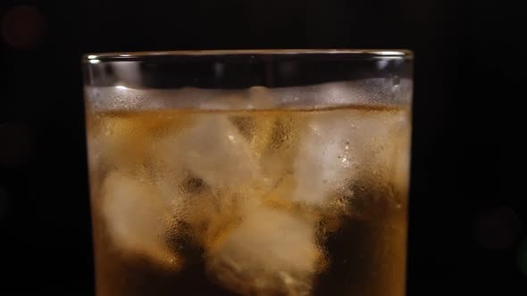 Closeup of a Full Glass of Whiskey with Ice Slowly Rotates on a Black Background
