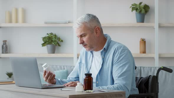 Disabled Senior Man Holding Medication Bottle Browsing Internet At Home