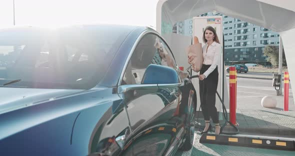 Beautiful Business Woman Approaches Her Electric Car With Groceries And Looks At