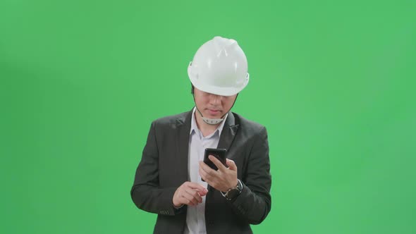 Asian Chief Engineer In The Hard Hat Use Mobile Phone While Walking On Green Screen Chroma Key