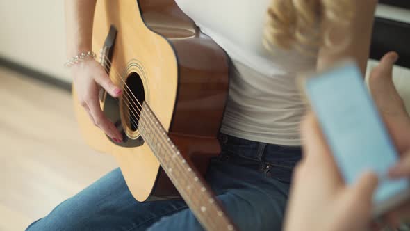 Close-up view of woman's hand  playing the classic acoustic guitar. Blonde girl is wearing white top